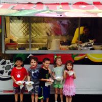 Kids smiling with food outside food truck.